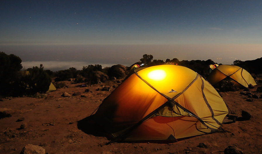 Orange tents camped on a sandy cliffside at night